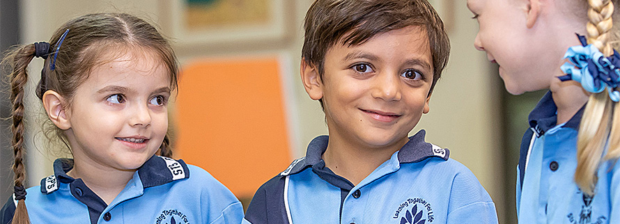 Three young students in school uniform standing together indoors and talking.